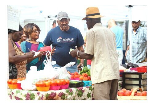 3 adults standing across each other at a table filled with baskets of vegetables at the downtown market Tallahassee